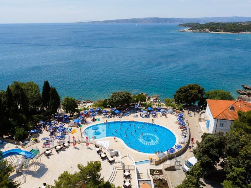 Piscina del hotel con tumbonas junto al mar y vista a la costa y el cielo.