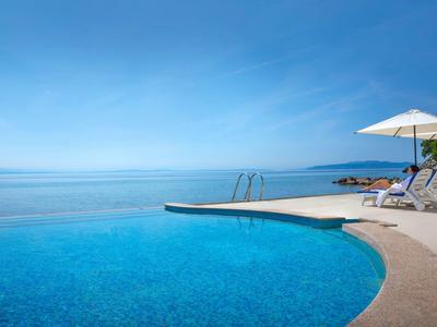 Infinity pool with sun loungers and umbrella overlooking the blue sea under clear sky.