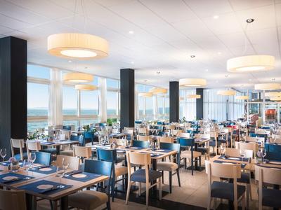 Spacious restaurant with blue set tables and large windows overlooking the water.