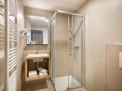 Compact bathroom with shower cabin, sink, and towel radiator in beige.