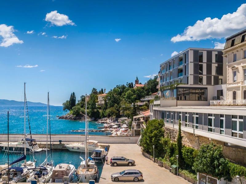 Harbor with sailboats beside modern and traditional buildings by the sea in sunny weather.