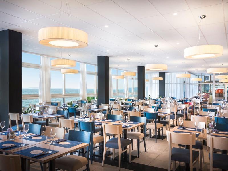 Spacious restaurant with blue set tables and large windows overlooking the water.