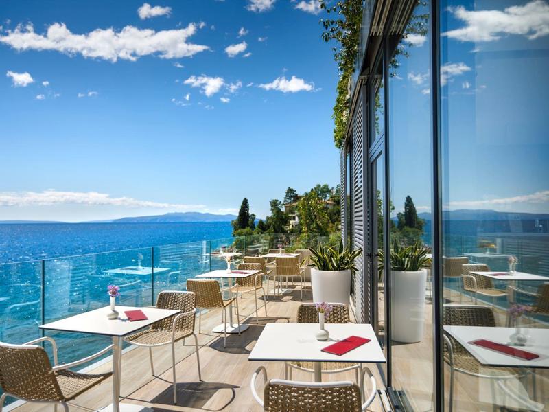 Terrace with tables and chairs overlooking the sea and mountains in sunny weather.