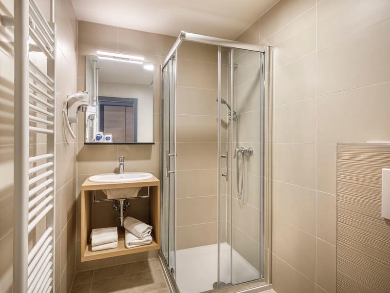 Compact bathroom with shower cabin, sink, and towel radiator in beige.