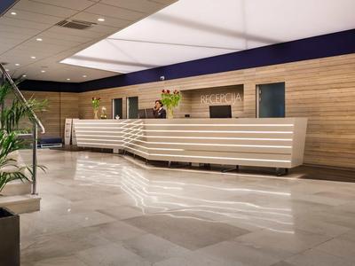 Moderner Hotel-Empfangsbereich mit hellem Marmorfußboden und großer Rezeption aus Holz.