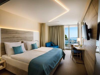 Modern hotel room with double bed, blue accents, and balcony with sea view.