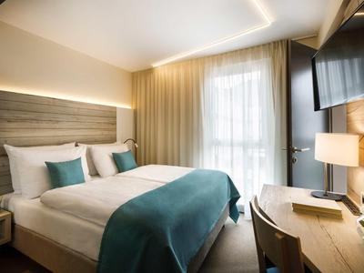 Modern hotel room with large bed, desk, and window with curtains.