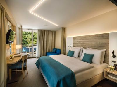 Modern eingerichtetes Hotelzimmer mit Doppelbett, Schreibtisch und Balkon mit Blick auf grüne Natur.