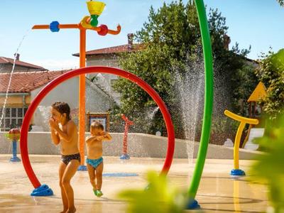 Children playing in a colorful water playground with various sprinklers and water fountains.