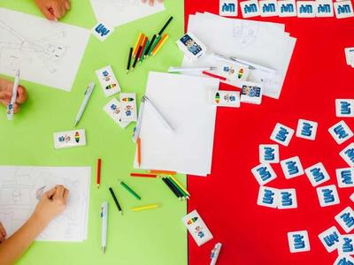 Children sit around a table writing on paper with pens and letter cards.