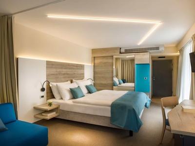 Modern hotel room with double bed, blue accents, and wall-mounted TV.