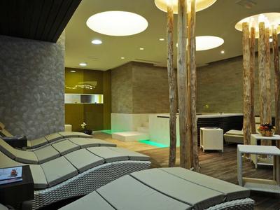 Modern indoor pool with lounge chairs and wooden logs in a hotel spa area.