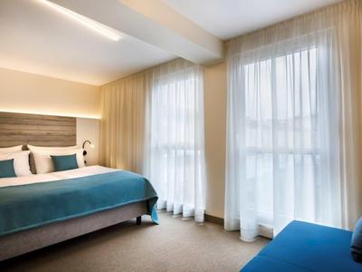 Modern hotel room with large bed, ample natural light, and bright curtains.