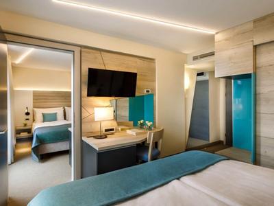 Modern hotel room with double bed, desk, TV, and wooden accents.