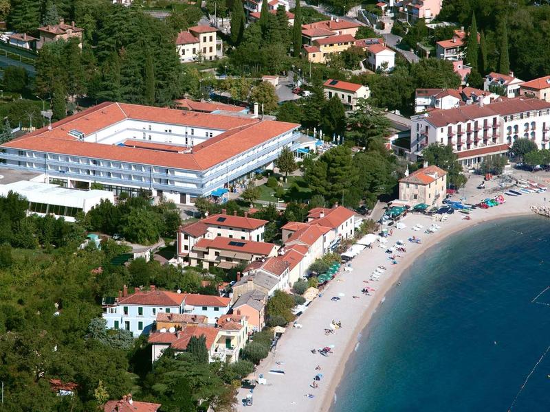 Aerial view of a hotel and beach with blue water and umbrellas along the coast.