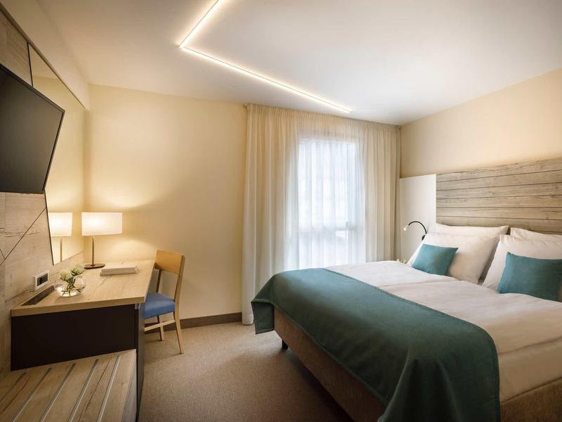 Modern hotel room with double bed, desk, TV, and soft lighting.