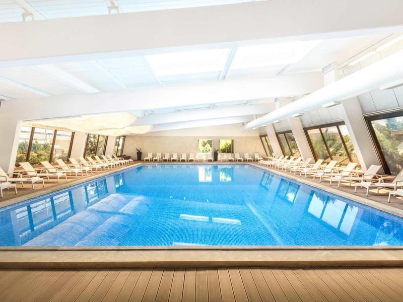 Bright indoor pool with large windows and lounge chairs on both sides.
