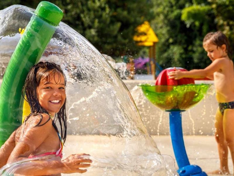 Children playing with a colorful water sprinkler outdoors on a sunny day.