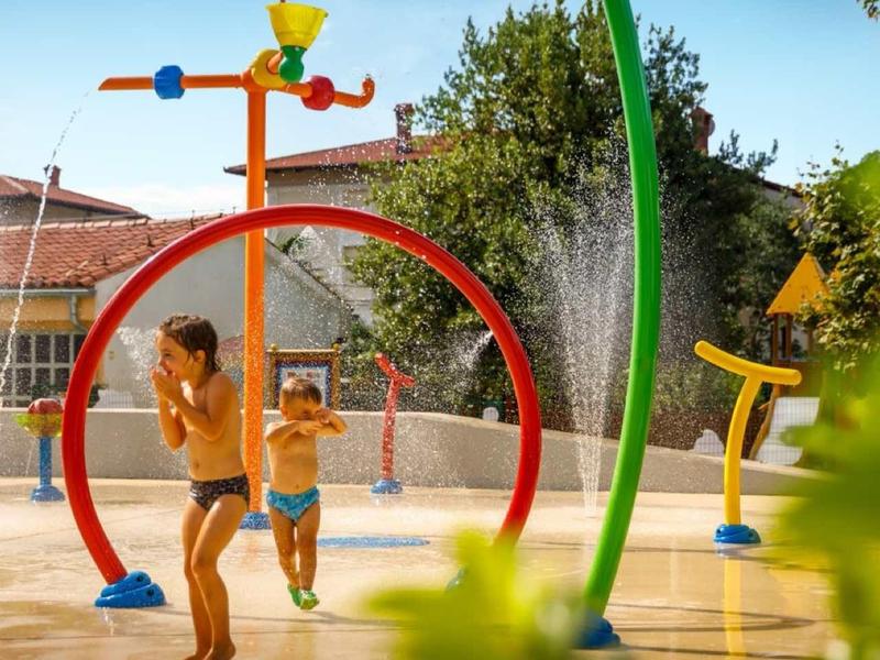Children playing in a colorful water playground with various sprinklers and water fountains.