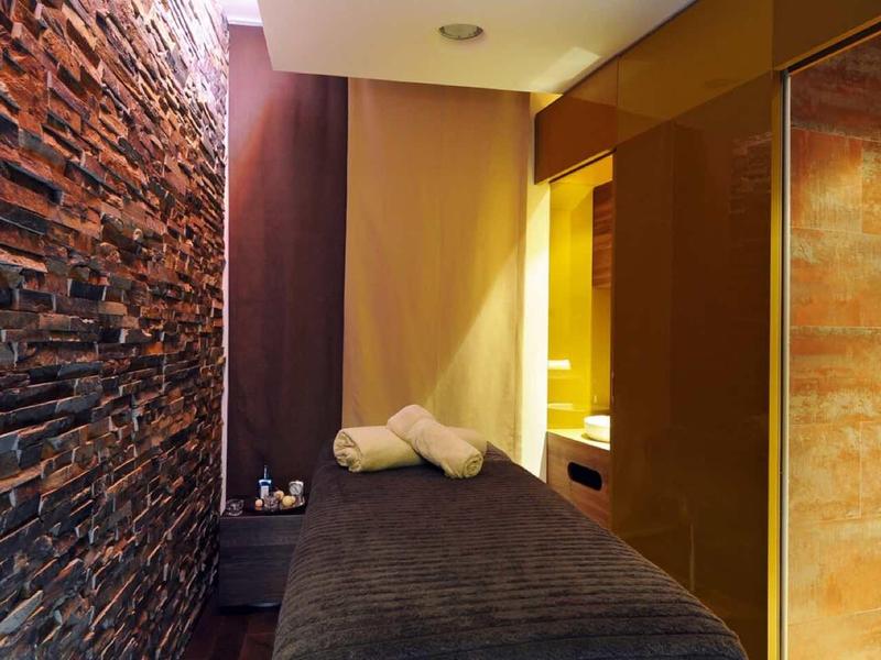Cozy spa room with massage table, decorative stone wall, and soft lighting.