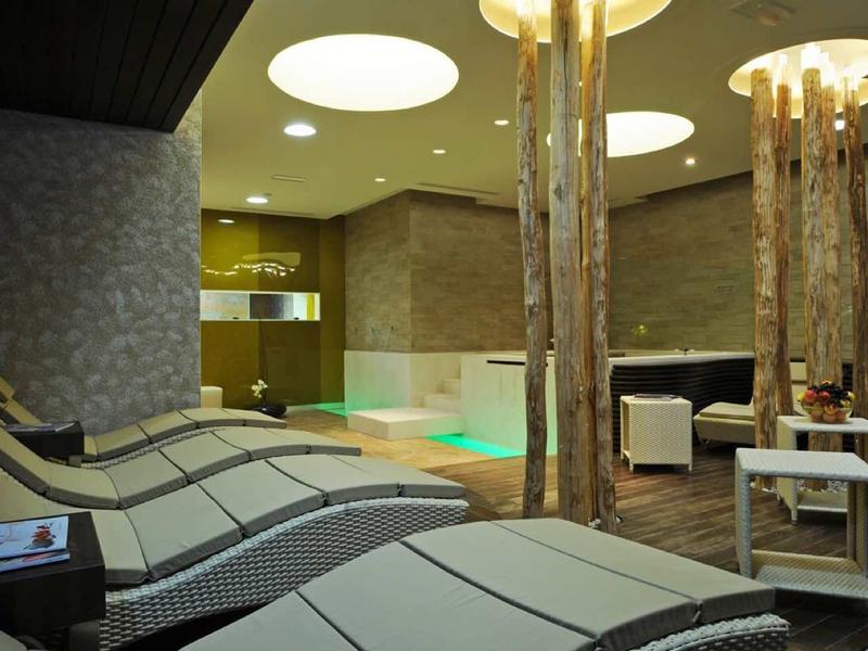 Modern indoor pool with lounge chairs and wooden logs in a hotel spa area.