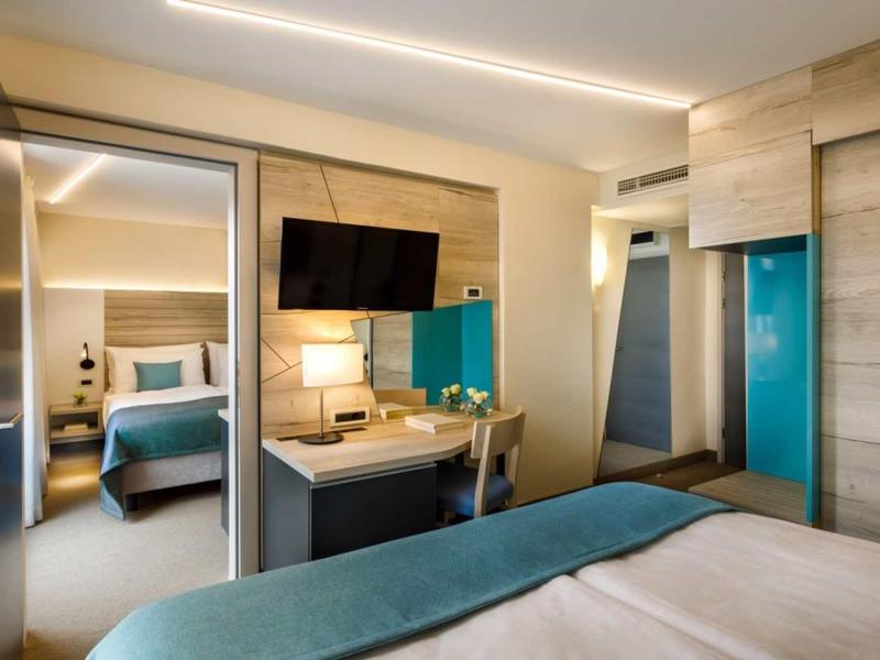 Modern hotel room with double bed, desk, TV, and wooden accents.