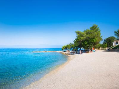 Strand mit klarem blauem Wasser, Bäumen und Sonnenschirmen unter blauem Himmel