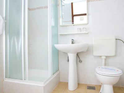 Kleines Badezimmer mit Duschkabine, Waschbecken und Toilette, heller Fliesenboden.