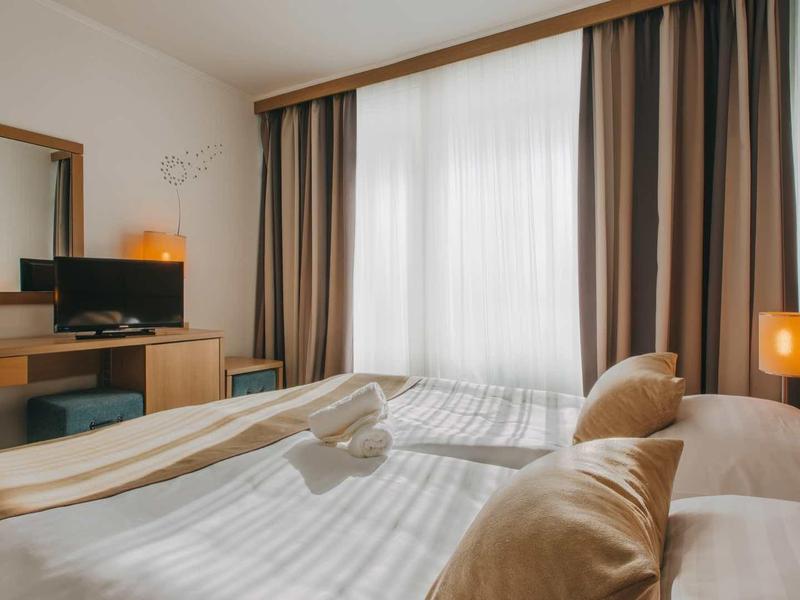 Brightly furnished hotel room with large bed, curtains, and TV on the dressing table.