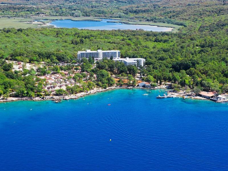 View of a coastal hotel surrounded by greenery and clear blue water.