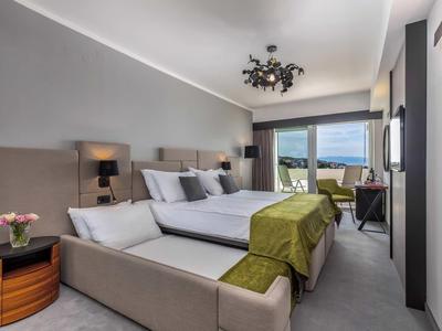 Modern hotel room with two beds, green bed runners, and large window overlooking the sea.