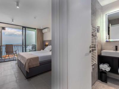 Modern hotel room with double bed, balcony overlooking the sea, and stylish bathroom.