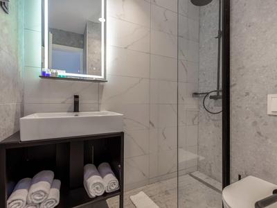 Modern bathroom with sink, illuminated mirror, glass-enclosed shower, and towels.