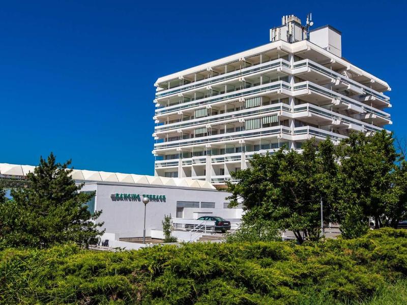 Tall hotel building with multiple balconies next to lower structure under a clear blue sky.