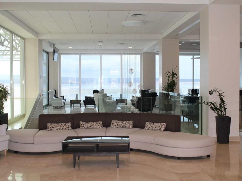 Bright hotel lounge with large curved sofa and expansive view through glass windows.