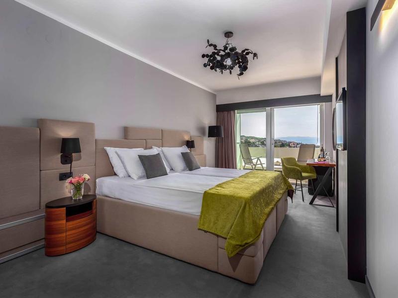 Modern hotel room with large bed, green bedspread, and mountain view.