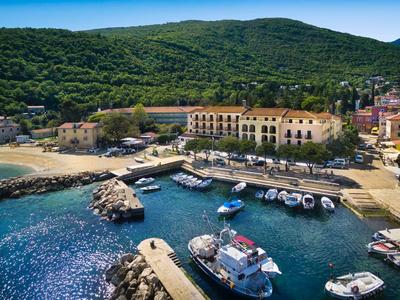 Small marina with boats by the coast and forested hill in the background.