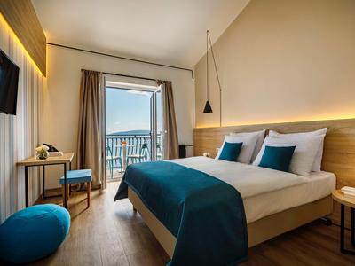 Modern hotel room with double bed, balcony, and sea view in daylight.