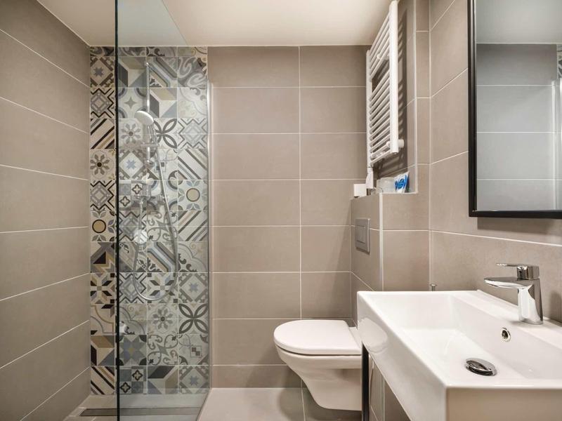 Modern bathroom with patterned shower, wall toilet, and white sink.