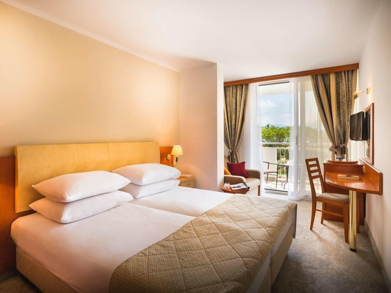 Helles Schlafzimmer mit Doppelbett, Schreibtisch, Fernseher und Balkon mit Bergblick.