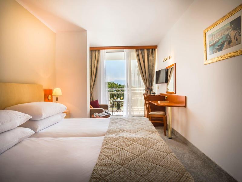 Helles Hotelzimmer mit Queensize-Bett, Schreibtisch, Sessel und Balkon mit Blick ins Grüne.