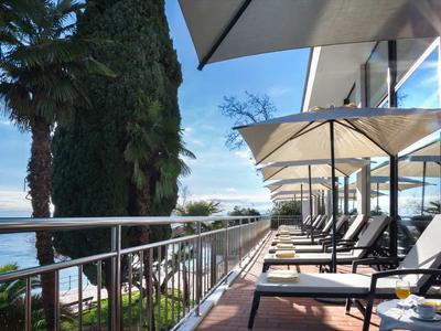 Balkon mit Liegestühlen und Sonnenschirmen, Palmen und Blick auf ruhiges blaues Meer.