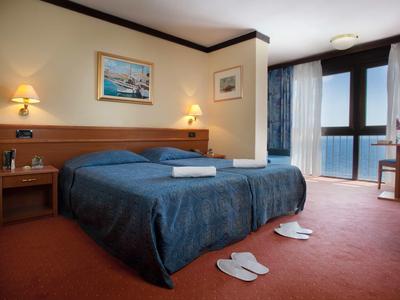 Hotelzimmer mit Doppelbett, Nachttischen, Bildern an der Wand und Balkon mit Vorhängen.