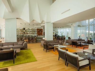 Lounge de hotel luminosa y moderna con sillones cómodos, suelo de madera y grandes ventanales.