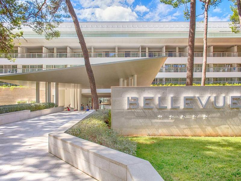 Modern hotel entrance with wide canopy and name written in concrete in front of the building.