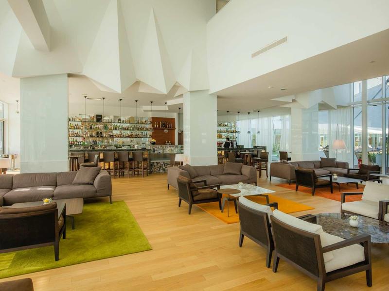 Bright hotel lounge area with modern sofas, armchairs, rugs, and large windows.