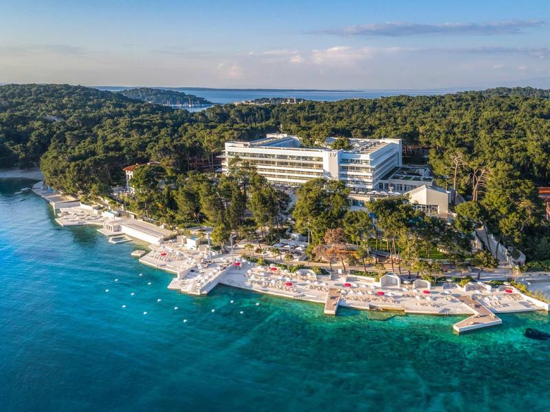 Hotel complex on a wooded coastline with terraces and access to clear blue sea.