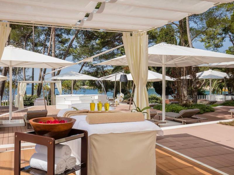 Terrace with sun umbrellas and cozy seating areas in a hotel garden overlooking trees.