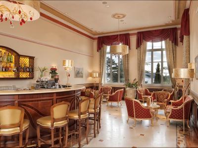 Elegante Bar mit Holztheke, Hockern und roten Sesseln in einem luxuriösen Hotelzimmer.