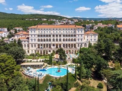 Großes historisches Hotel mit Pool in einer grünen, hügeligen Landschaft unter blauem Himmel.